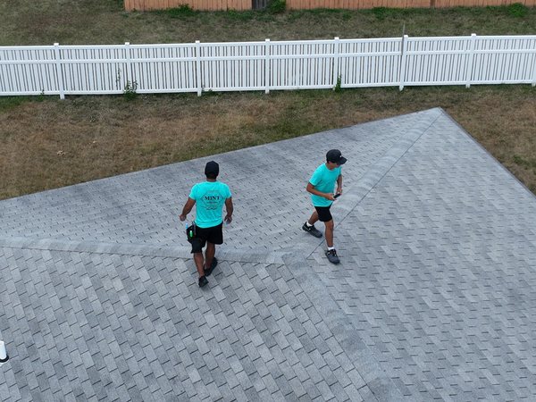 Two Mint Exteriors crew in teal shirts walking a roof during an inspection